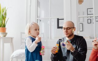 A joyful moment between a father and daughter blowing bubbles indoors, highlighting family fun.