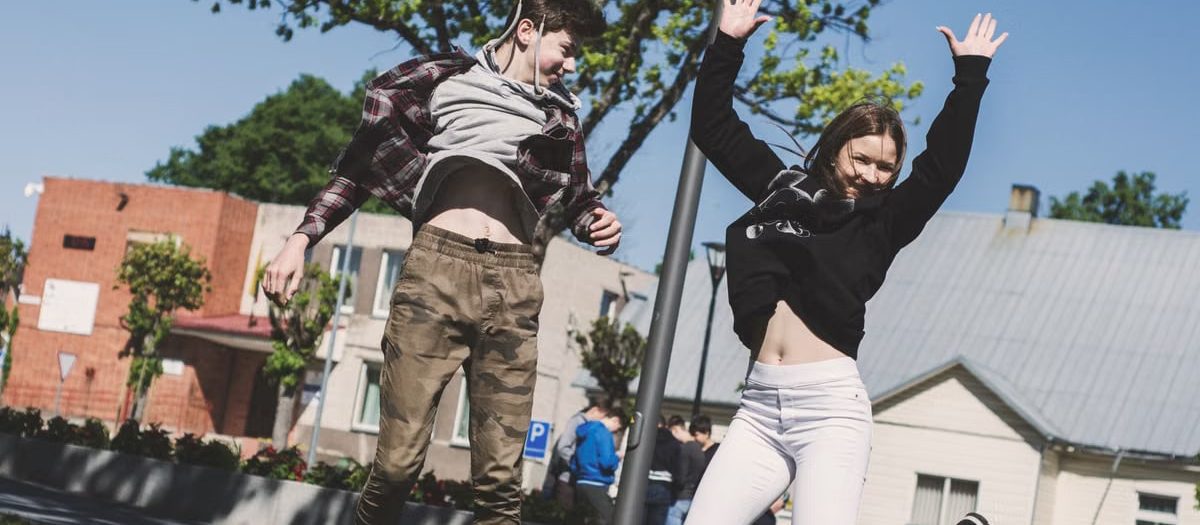 Two teenagers joyfully jumping outdoors in Šiluva, Lithuania under a bright blue sky. Captured in springtime.