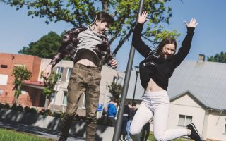 Two teenagers joyfully jumping outdoors in Šiluva, Lithuania under a bright blue sky. Captured in springtime.